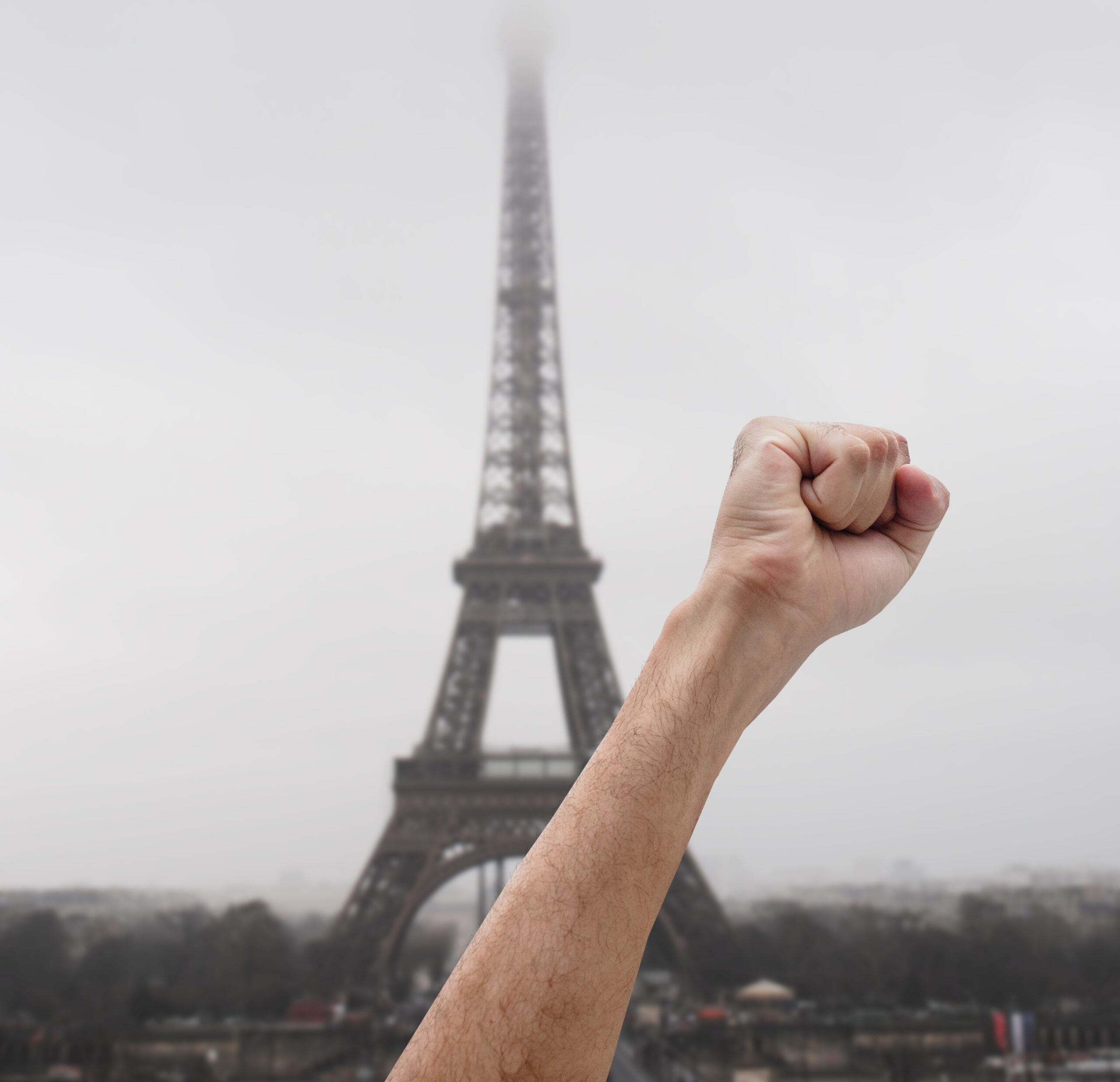 Eine im Protest erhobene Faust vor dem, im Hintergrund sichtbaren, Eiffelturm in Paris.